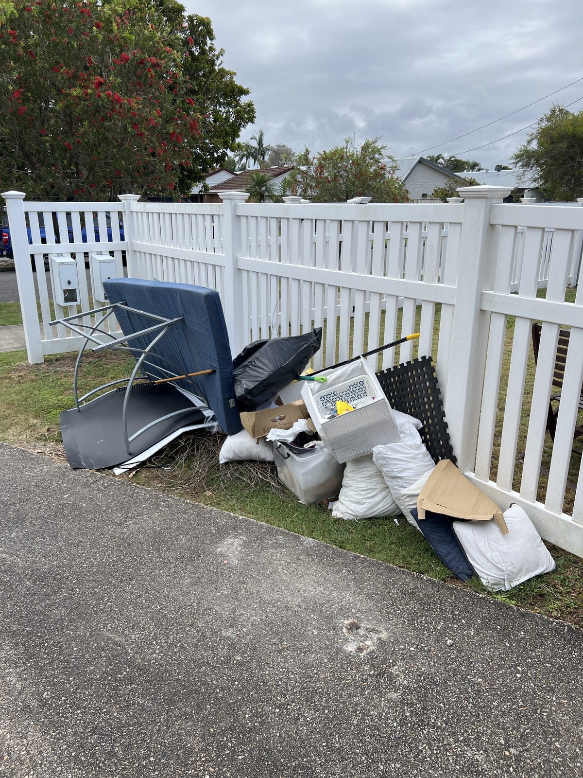 Old furniture and household rubbish piled beside a fence, ready for collection
